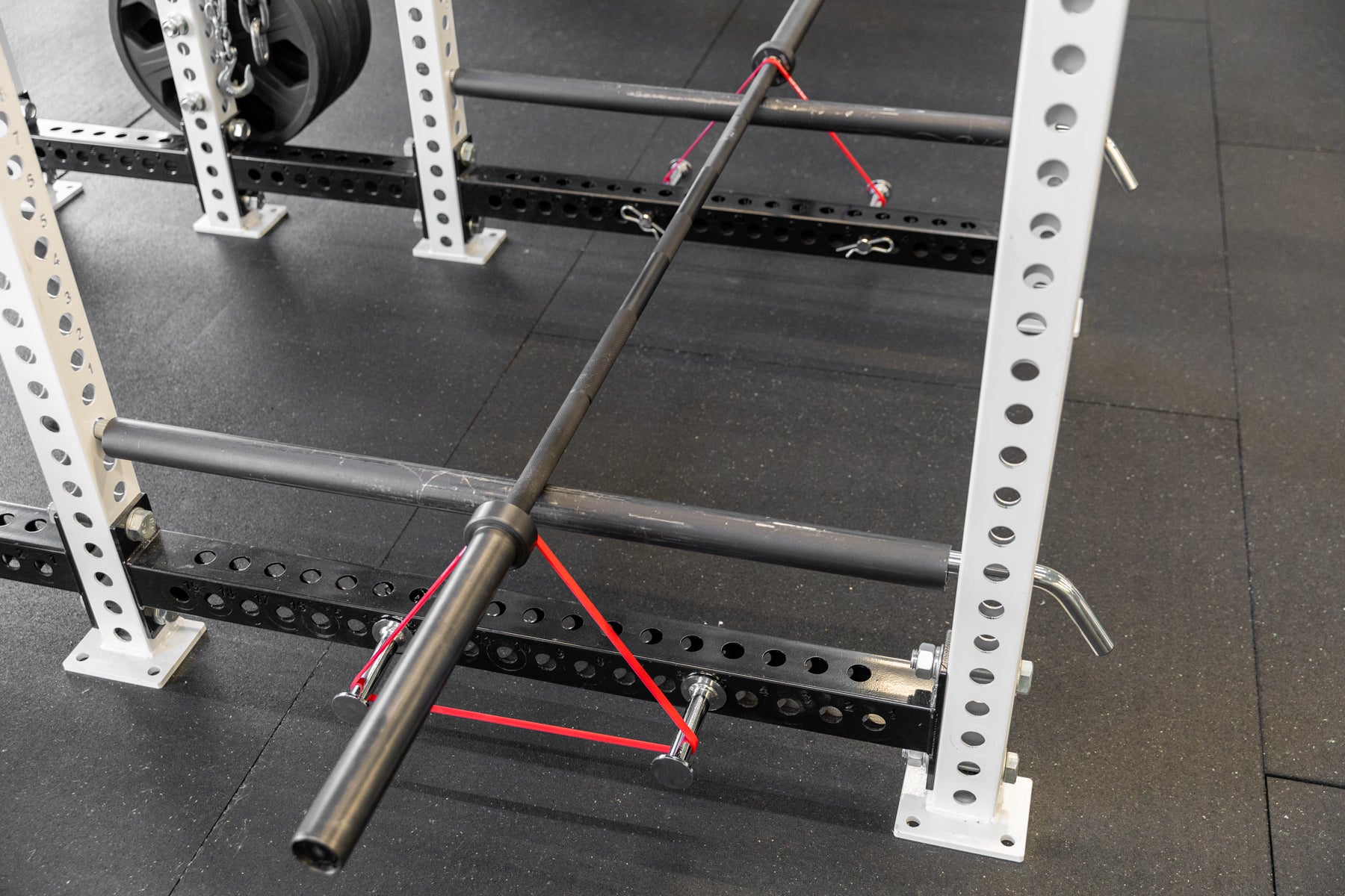 Empty barbell on pin-pipe safeties with red short resistance bands attached using band pegs for banded bent over rows.