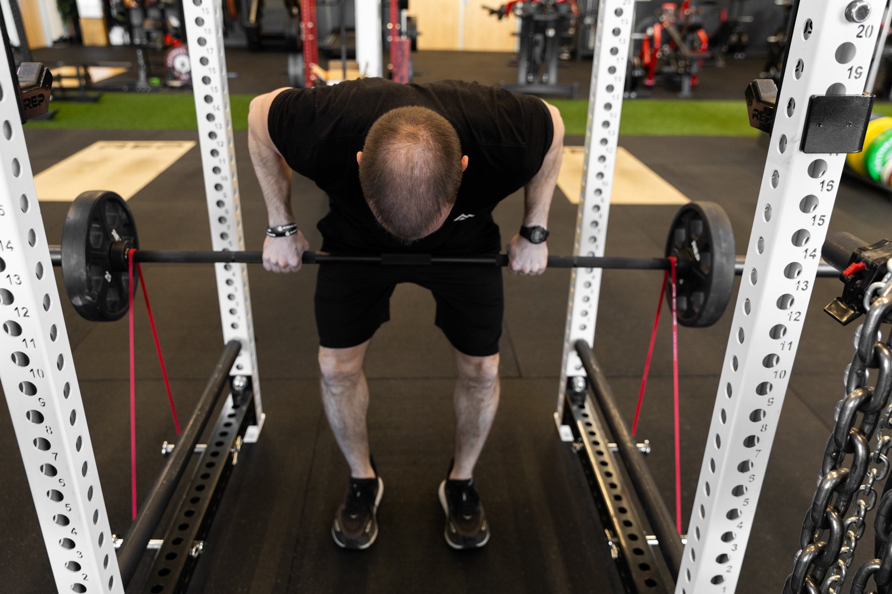 Lifter performing bent over rows with a barbell loaded with a pair of 25lb plates and a pair of red short resistance bands for added resistance.