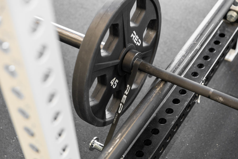 Close-up view of a barbell loaded with a 45lb plate and a black short resistance band for added resistance.