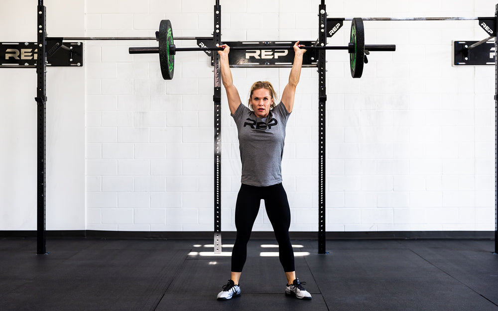 Female lifter holding a loaded REP 15kg Colorado Bar in the overhead position.