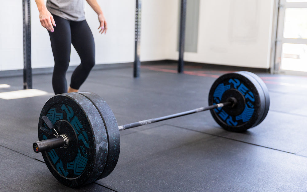 Female lifter approaching a REP 15kg Colorado Bar that is on the ground and loaded with two pairs of 45lb REP Pinnacle Plates.