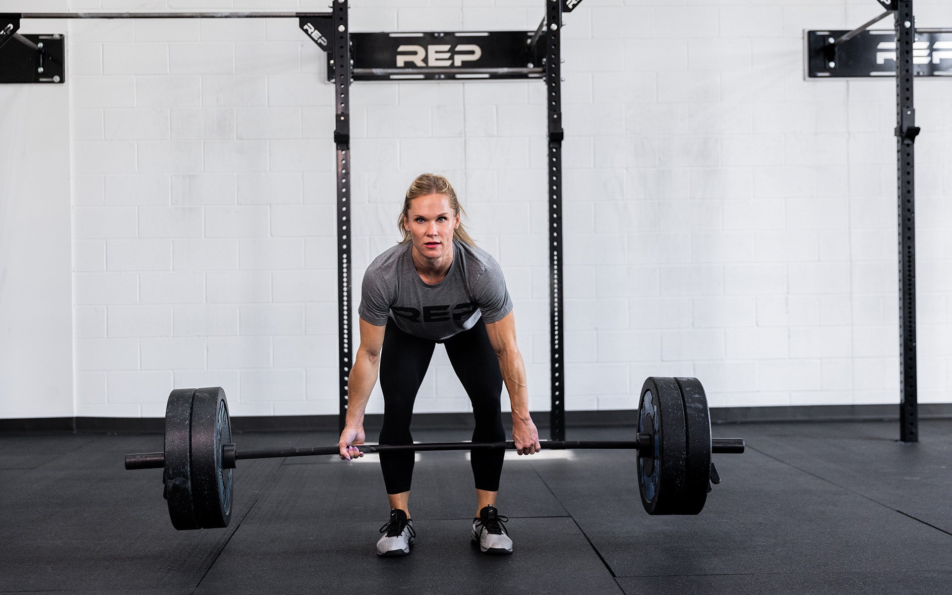 Head on view of a female lifter performing a deadlift with a REP 15kg Colorado Bar loaded with two pairs of 45lb REP Pinnacle Plates.