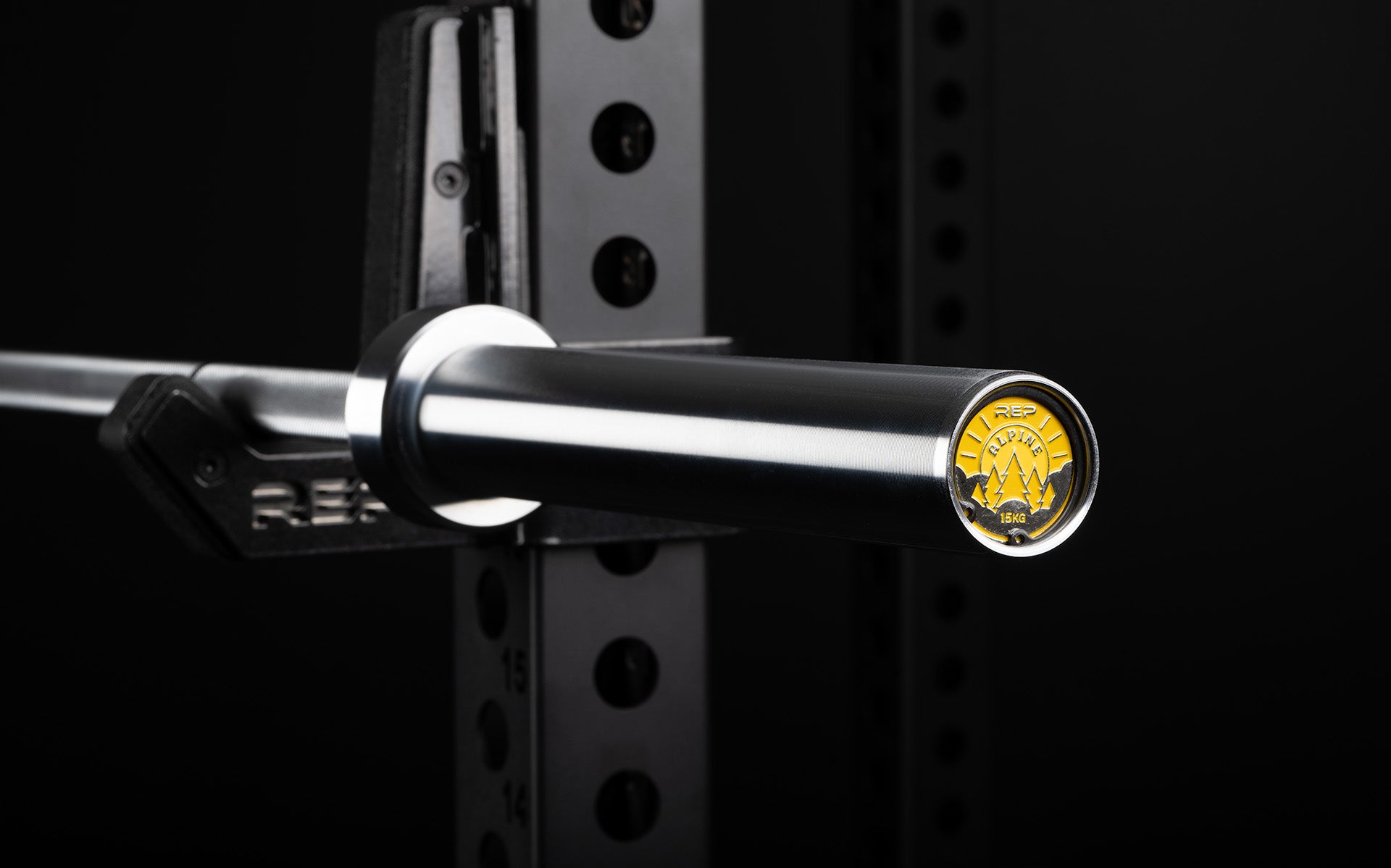 Close-up view of the sleeve and premium endcap of a racked REP 15kg Alpine Weightlifting Bar.
