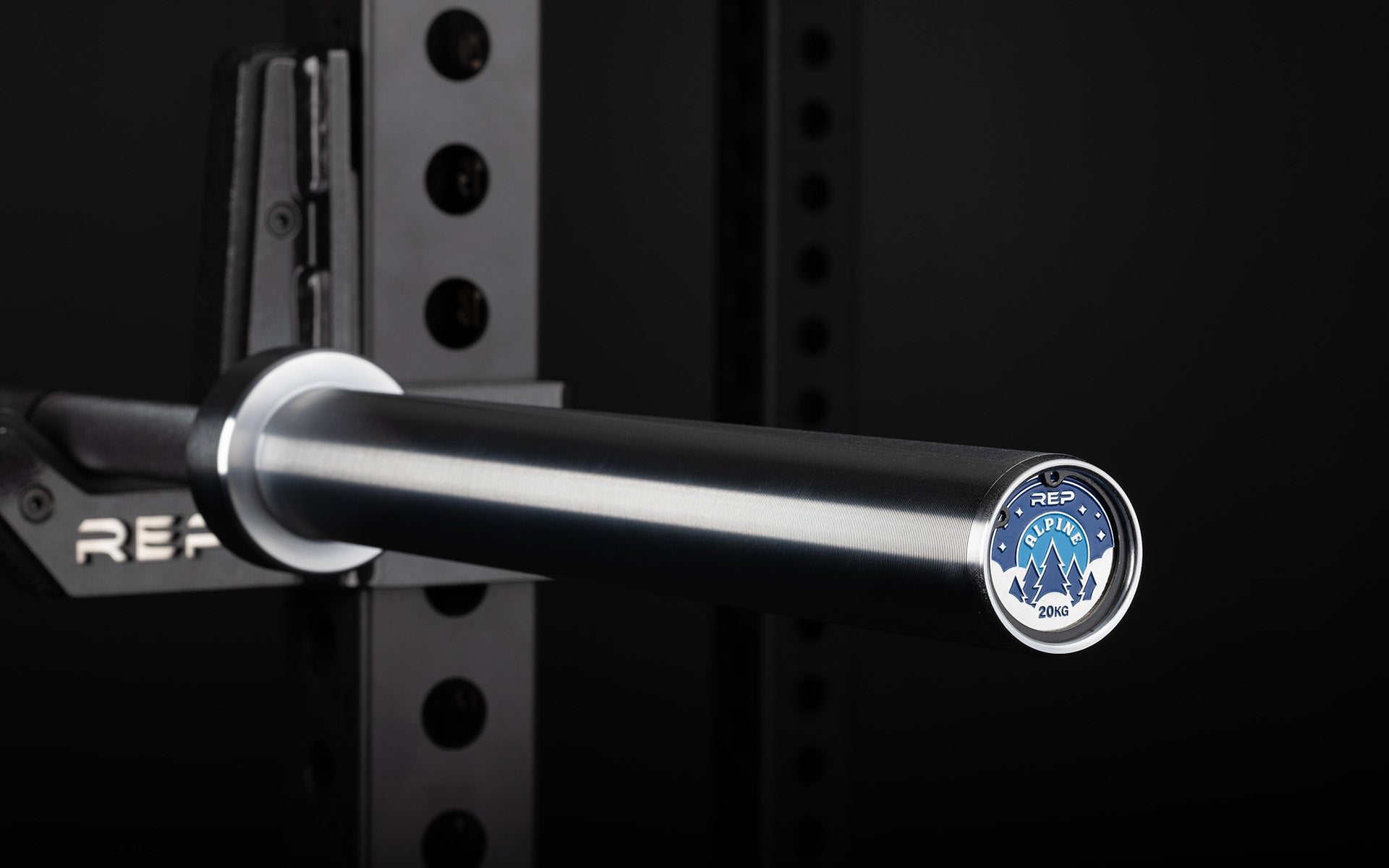 Close-up view of the sleeve and premium endcap of a racked REP 20kg Alpine Weightlifting Bar.