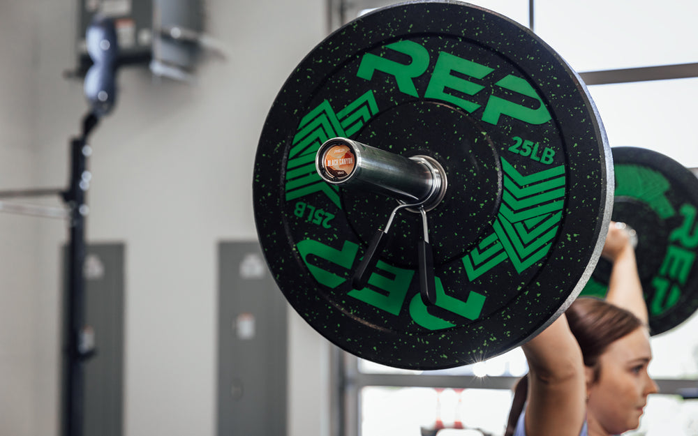 Female lifter in the finish position of a snatch using a REP 15kg Black Canyon Bar.