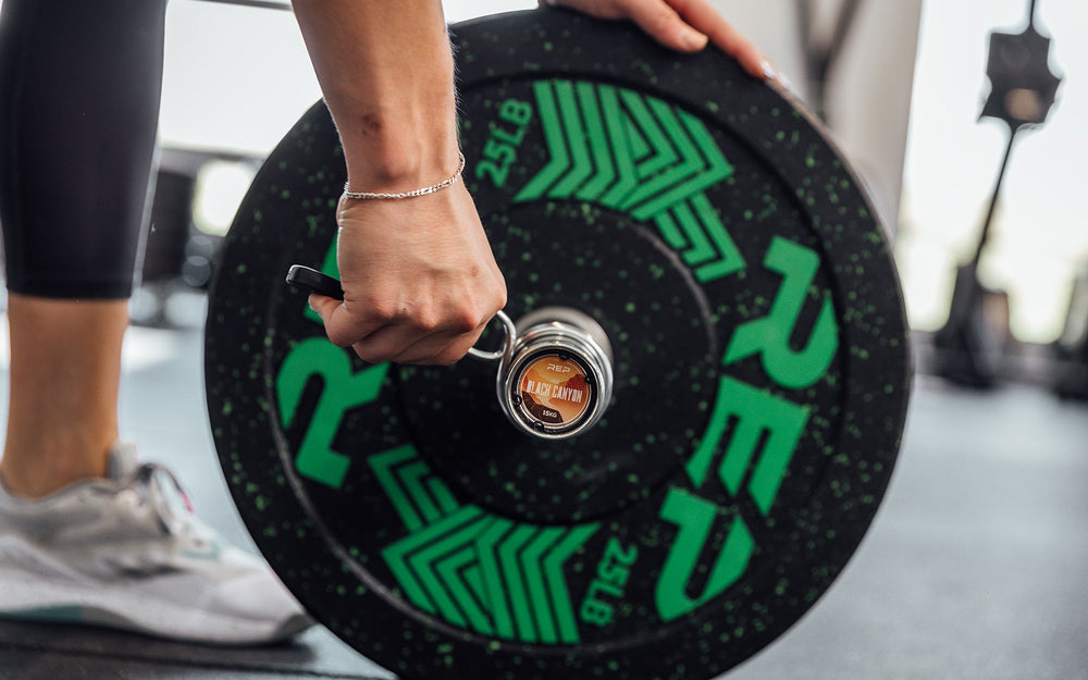 Close-up view of a female lifter putting on a spring clip to secure a 25lb plate to the REP 15kg Black Canyon Bar.