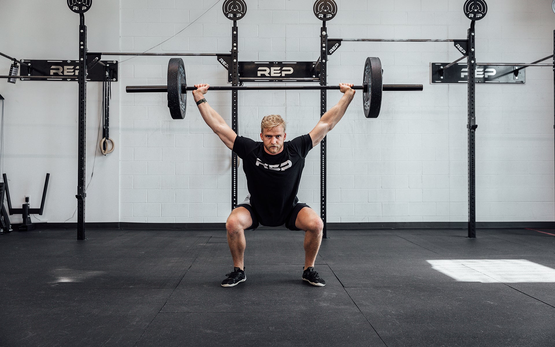 Male lifter performing an overhead squat with a loaded REP Black Canyon Bar - 20kg.