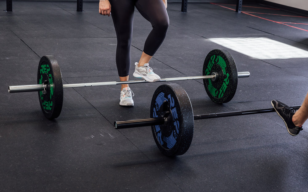 Two loaded REP Black Canyon Bar - 20kg's on the stall mats of a gym floor.