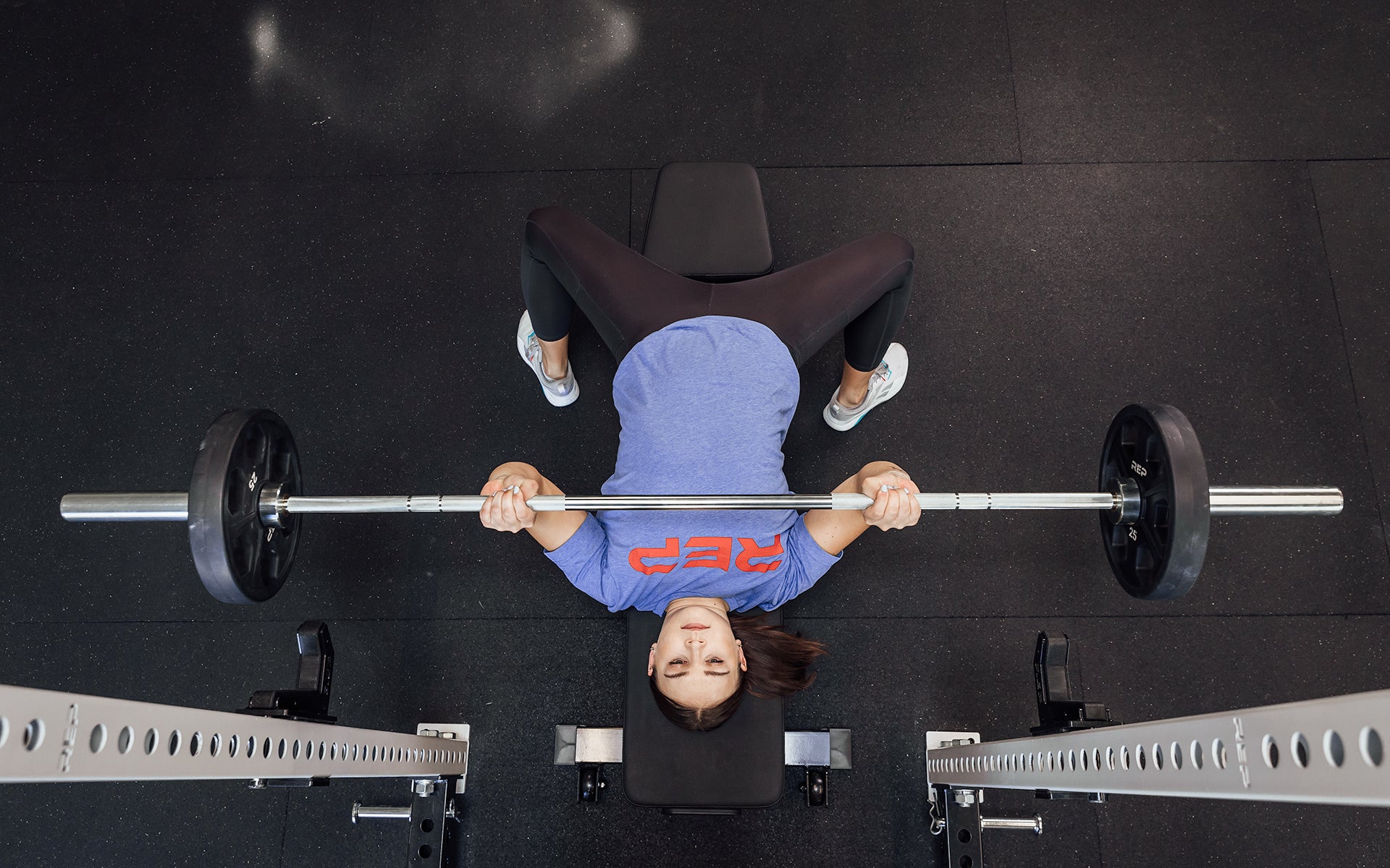 Overhead view of a female lifter performing a bench press with a loaded REP 15kg Black Canyon Bar.