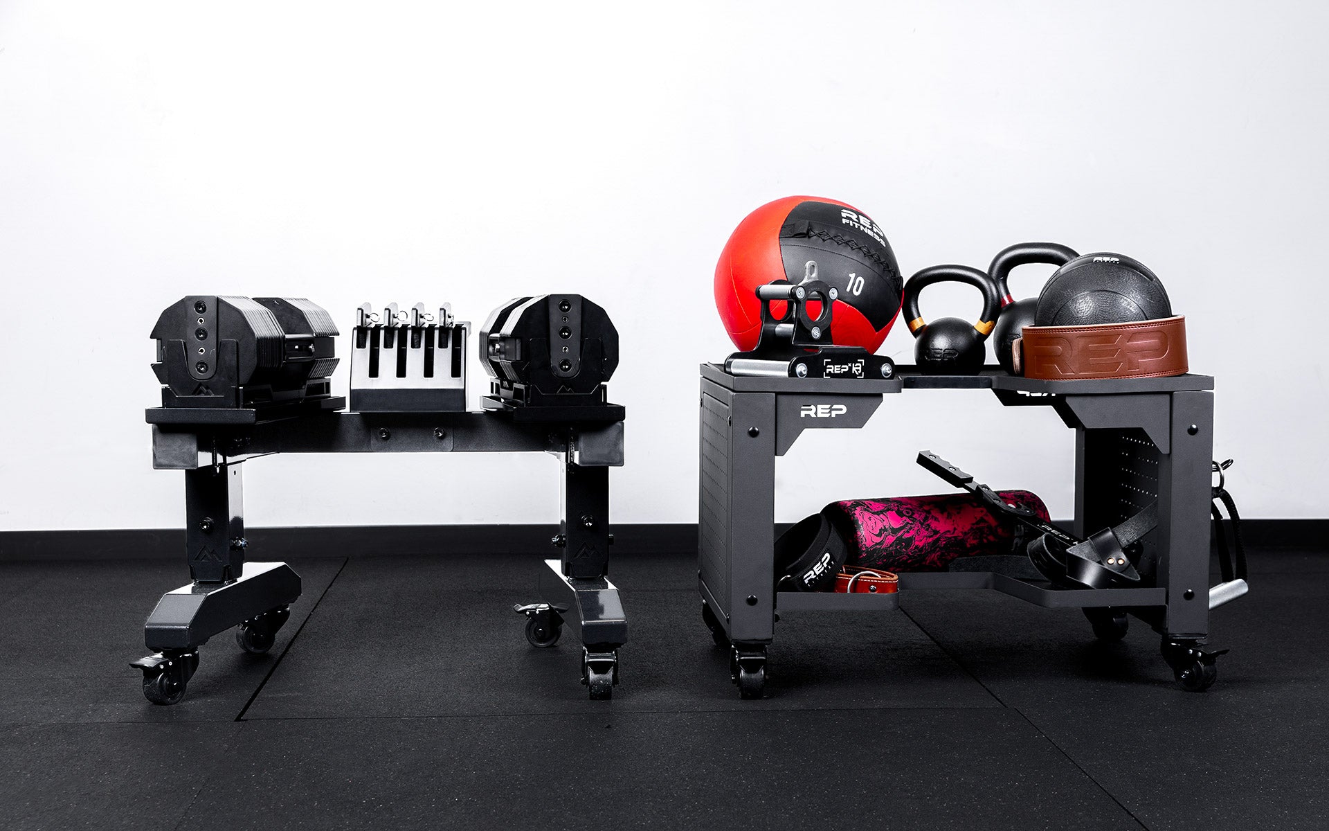 Metallic black REP® Adjustable Dumbbell Stand with REP® x PÉPIN™ adjustable dumbbells next to a matte black Dumbbell Storage Cart loaded with various workout equipment.