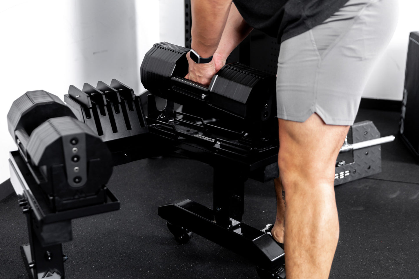 Athlete picking up REP® x PÉPIN™ adjustable dumbbells from a metallic black REP® Adjustable Dumbbell Stand from one side