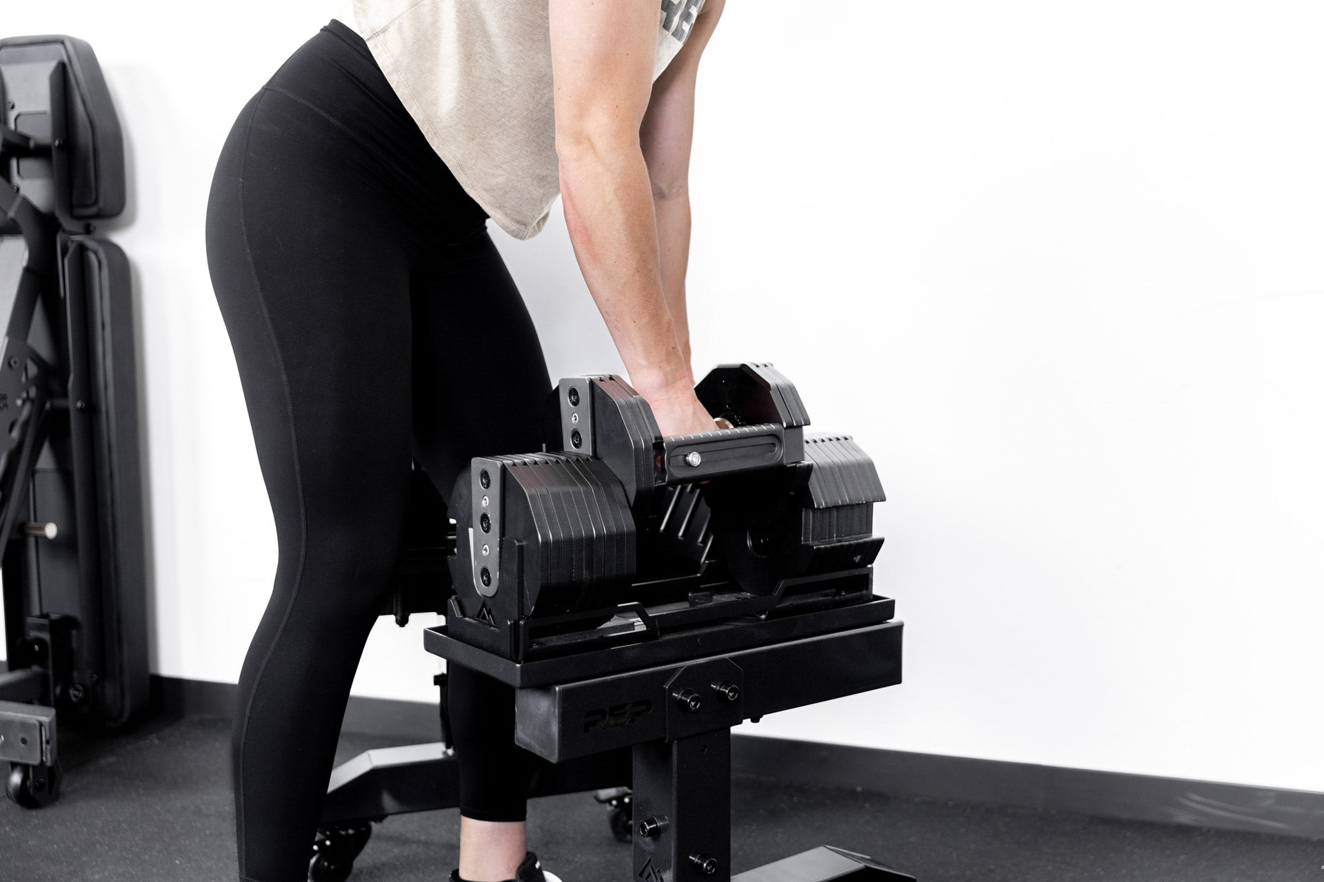 Athlete lifting up REP® x PÉPIN™ adjustable dumbbells from a metallic black REP® Adjustable Dumbbell Stand.