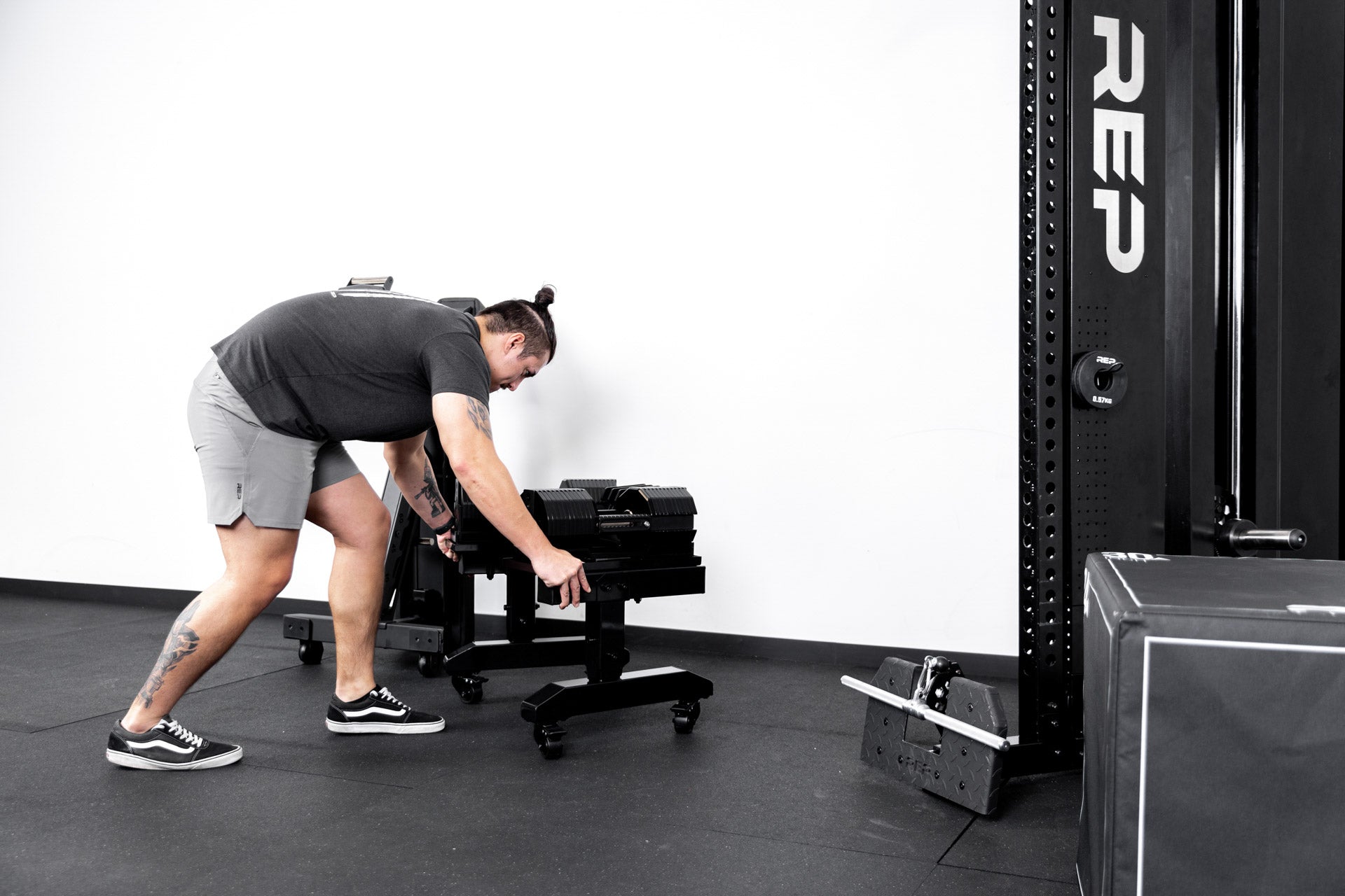 Athlete moving a metallic black REP® Adjustable Dumbbell Stand using the attached caster wheels.