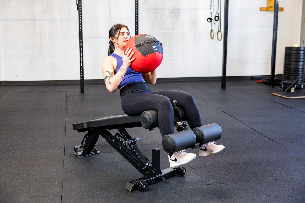 Athlete doing sit ups with the Adjustable Bench Leg Roller Attachment 2.0 and a medicine ball