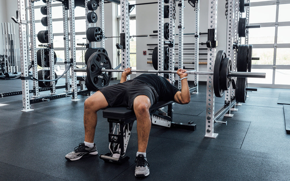 Male lifter performing a bench press with a loaded REP Delta Basic Bar.