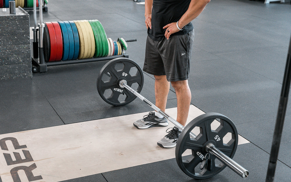 Male lifter standing above a loaded REP Delta Basic Bar on an Olympic lifting platform.