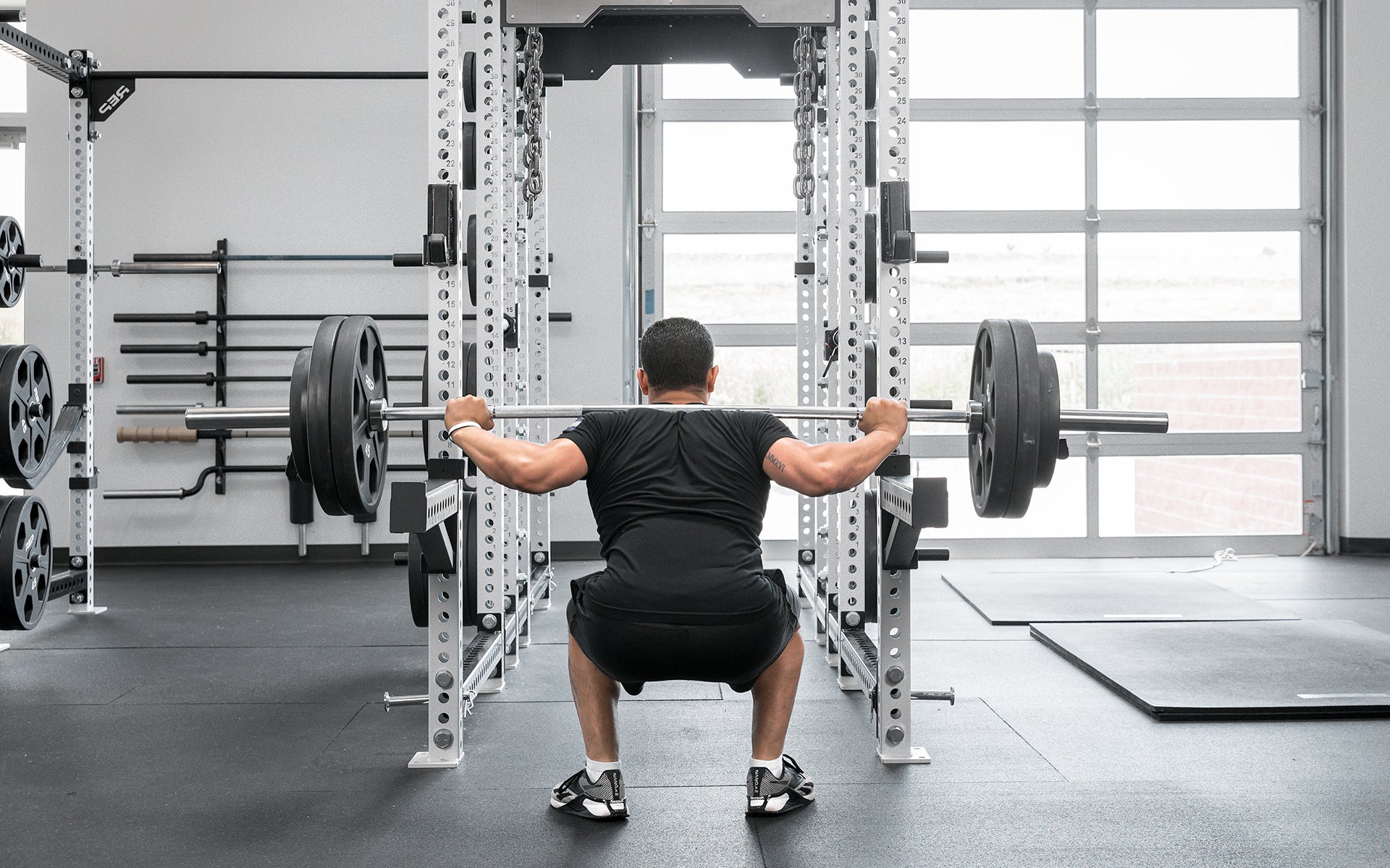Male lifter performing a back squat with a loaded REP Delta Basic Bar.