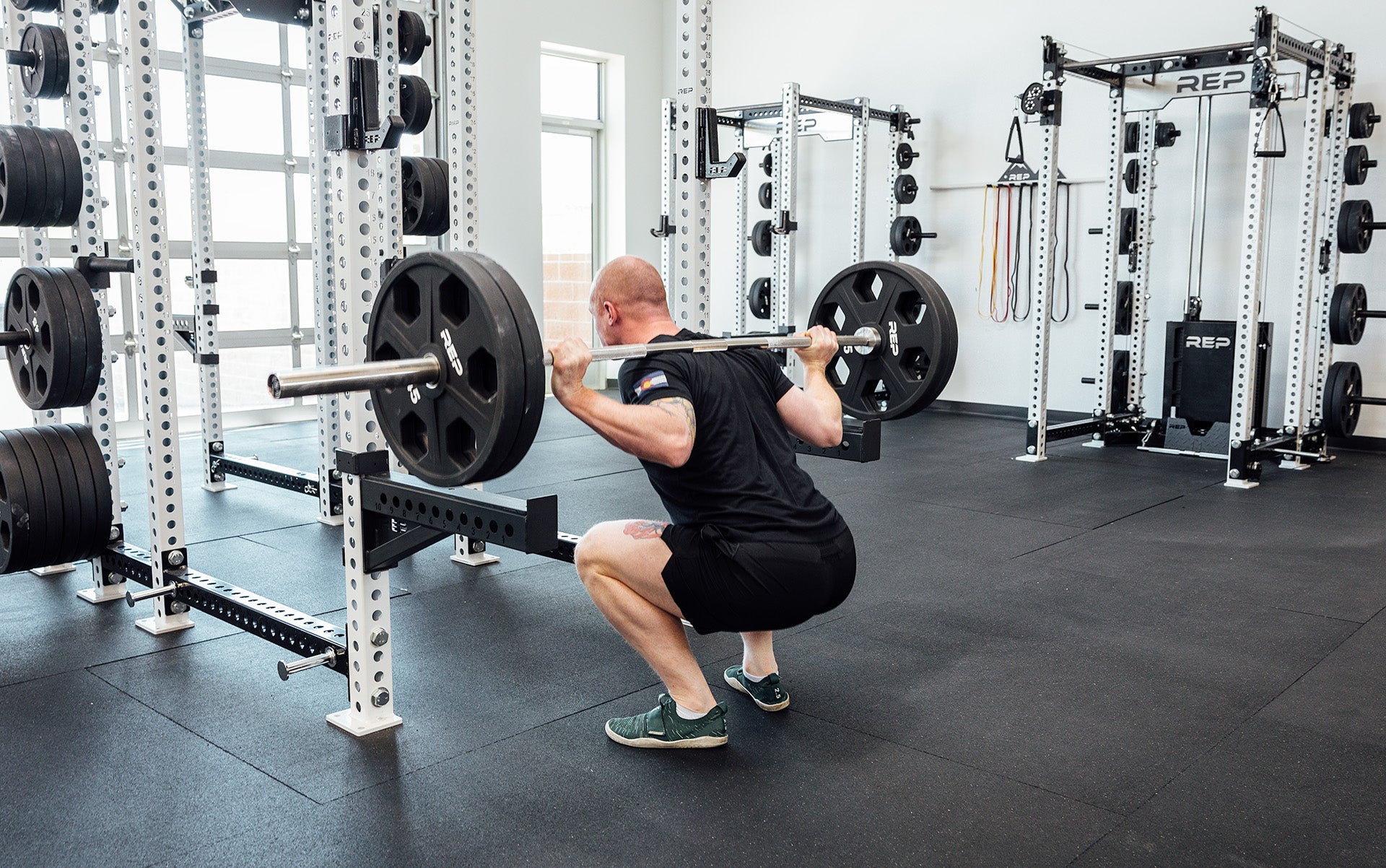 Male lifter in the bottom of a back squat with a loaded REP Double Black Diamond Power Bar.