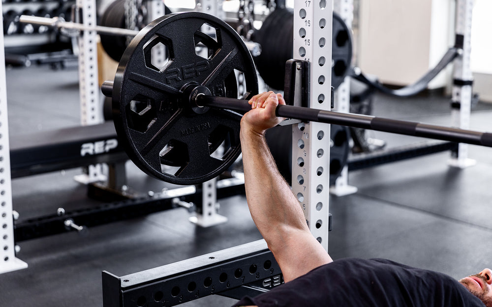 Lifter performing a bench press with a barbell loaded with a pair of 45lb and 25lb USA-Made Equalizer Iron Plates.