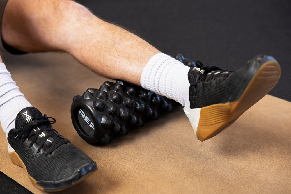 Person using High Density Foam Roller to roll out calf on a cork yoga mat.