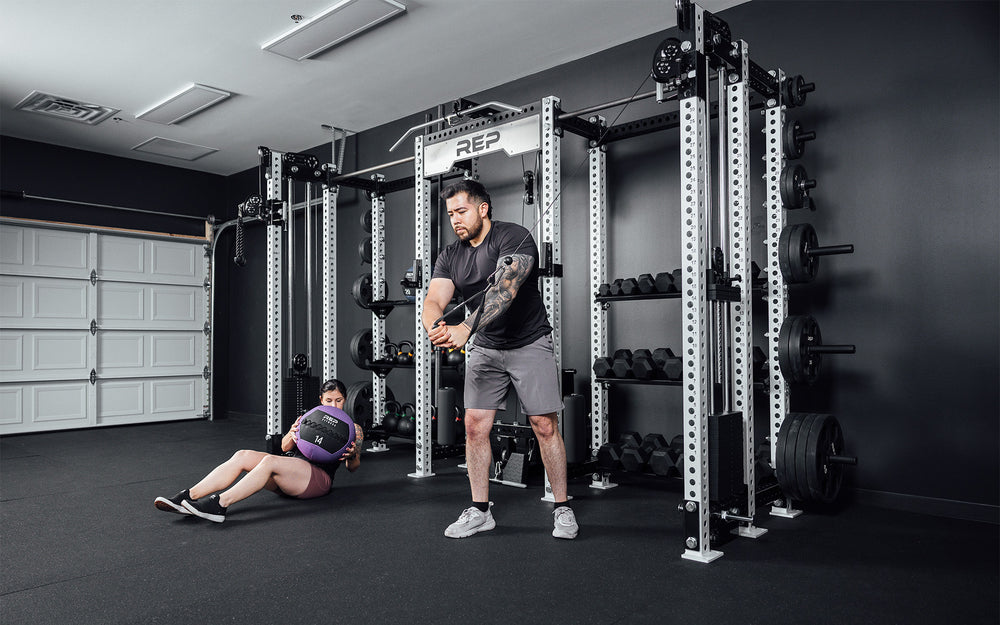 2 athletes training on Hyperion series 1. One using cables on the right side while the other uses med balls on left.