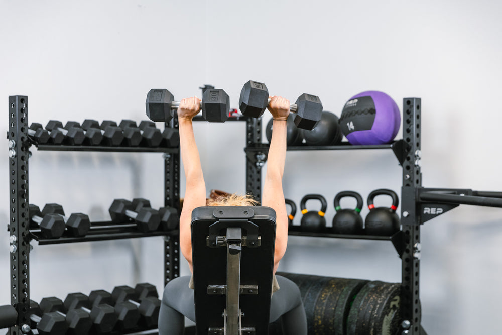 Someone using hex dumbbells in front of Corner Shelf Stand-Alone Storage System and dumbbell shelves