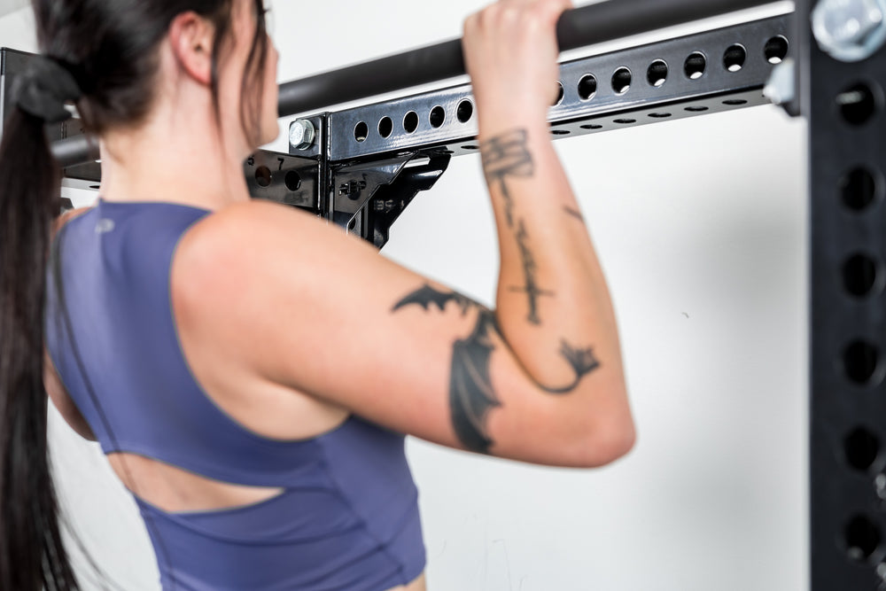 Person in a blue athletic top performing pull-ups on a bar with the compact Logo Plate Crossmember 2.0 being shown in the back. 