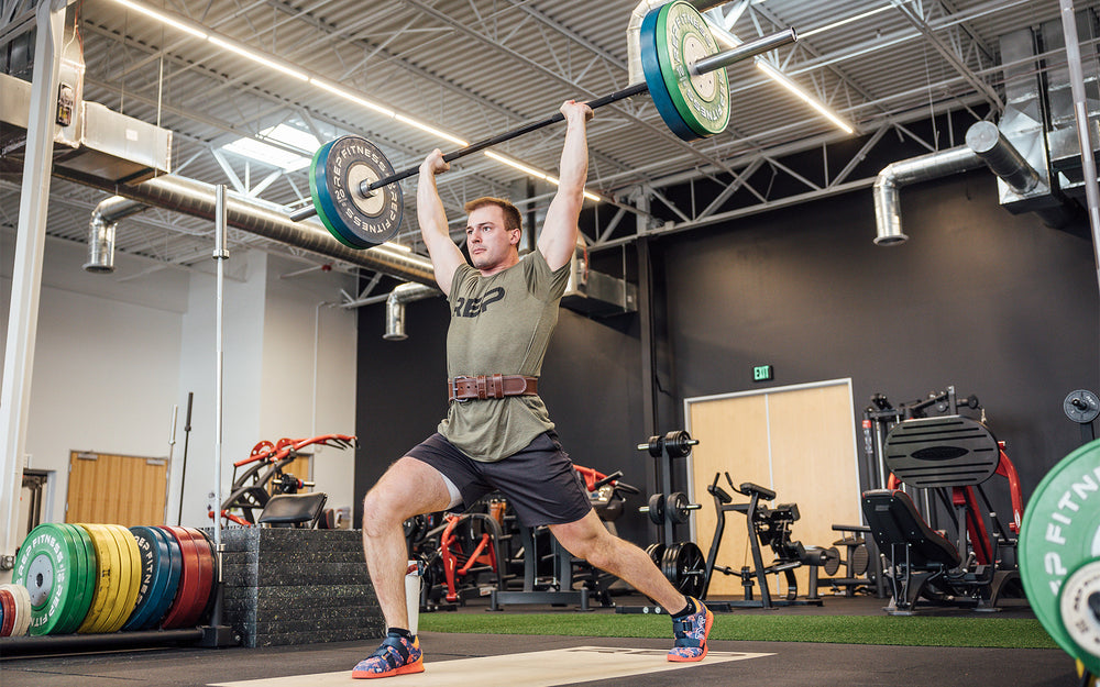 Athlete in the split jerk position of a clean and jerk while wearing a brown REP Leather Olympic Lifting Belt.