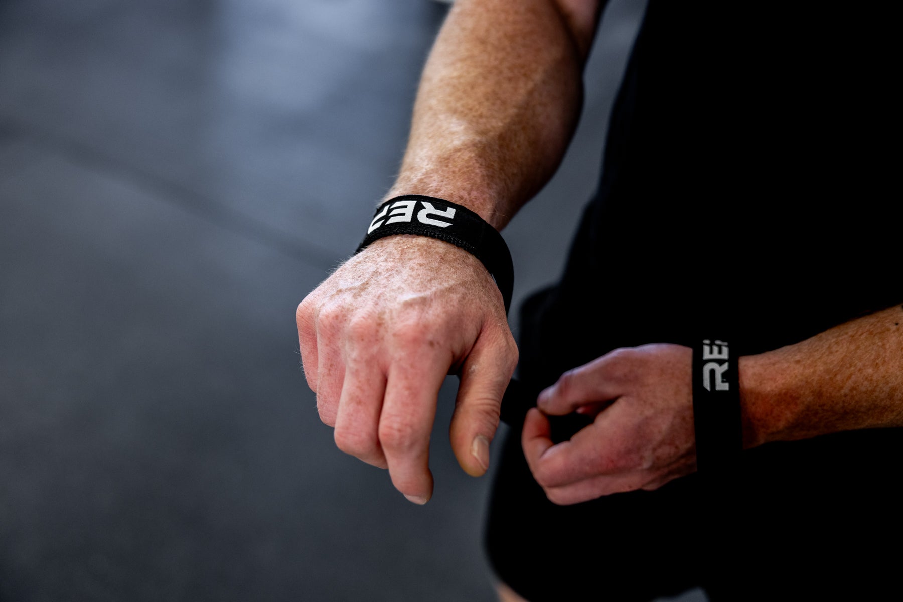 Close-up view of an athlete putting on a pair of black REP Olympic Lifting Straps.