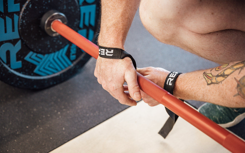 Close-up view of an athlete securing the right-sided black REP Olympic Lifting Strap to a loaded barbell.