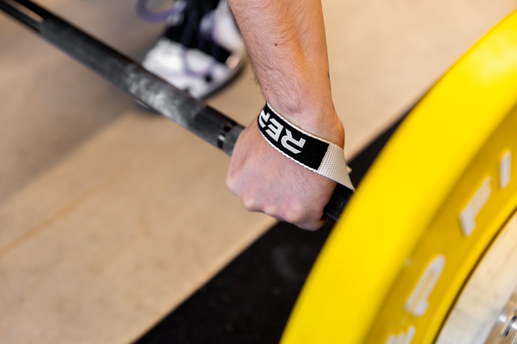 Close-up view of an athlete securing the left-sided white REP Olympic Lifting Strap to a loaded barbell.