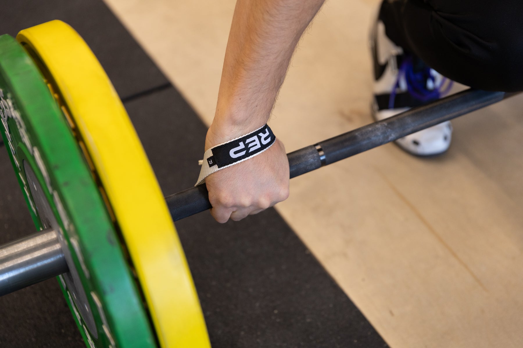 Close-up view of an athlete securing the right-sided white REP Olympic Lifting Strap to a loaded barbell.