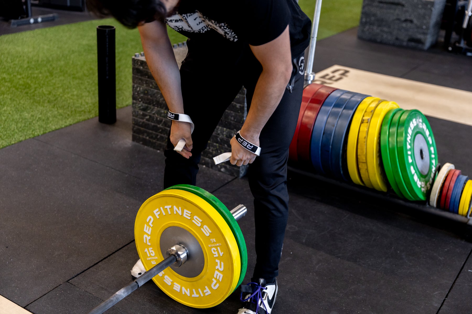 Athlete getting ready to unload a barbell while wearing a pair of white REP Olympic Lifting Straps.