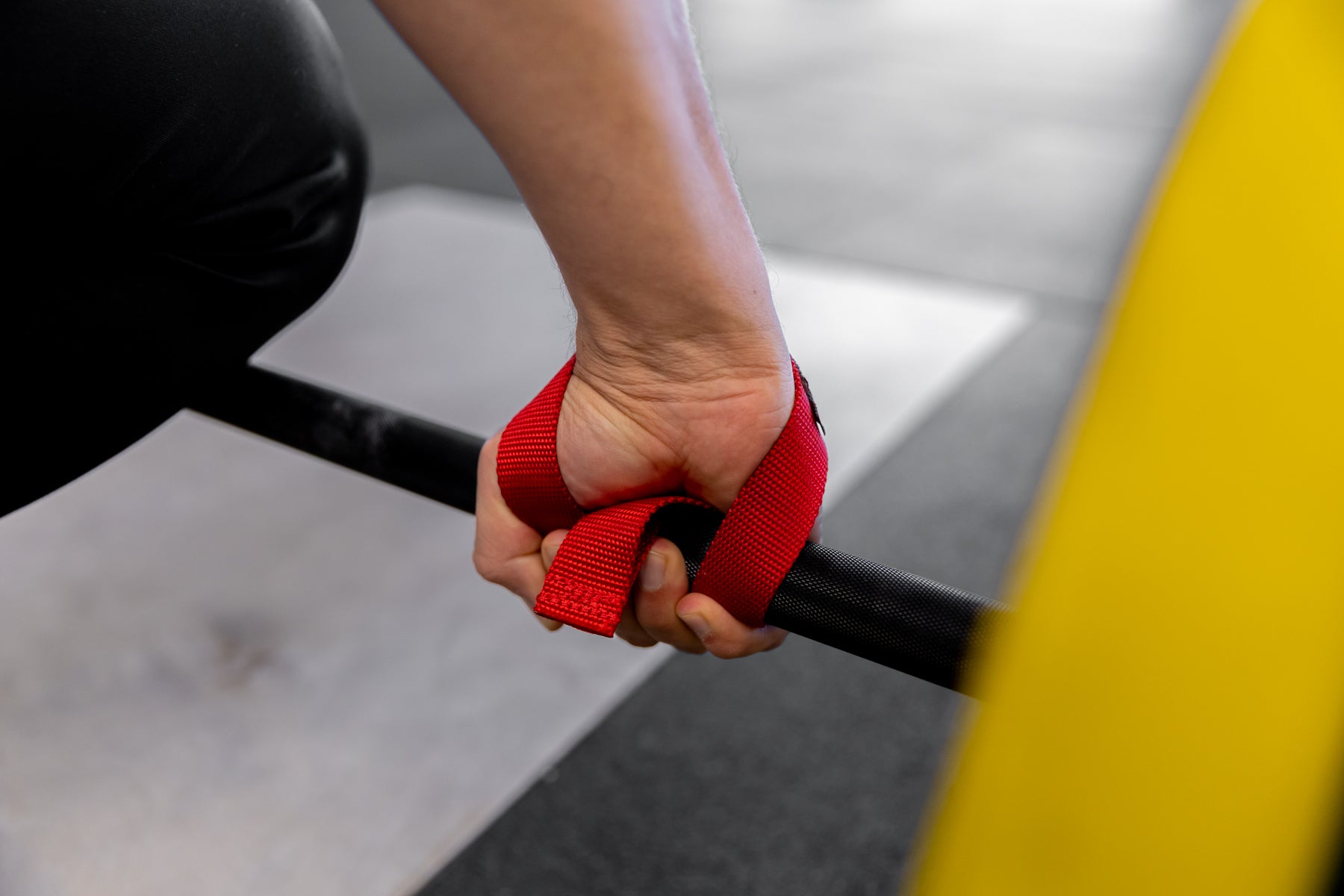 Close-up view of an athlete securing the right-sided red REP Olympic Lifting Strap to a loaded barbell.