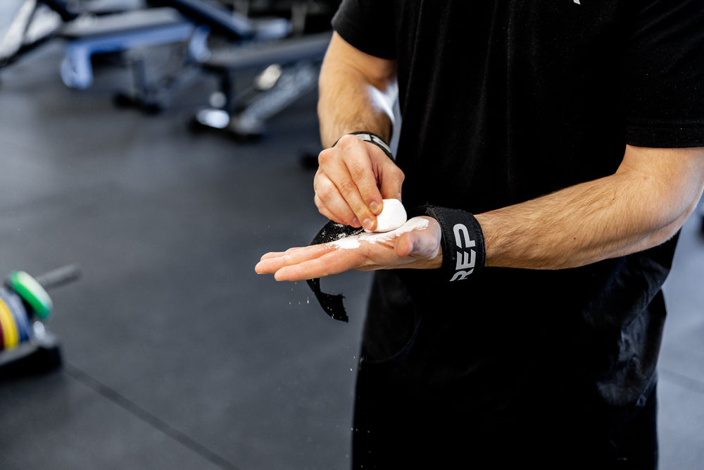 Lifter applying chalk to his hand wile wearing REP Lifting Straps.