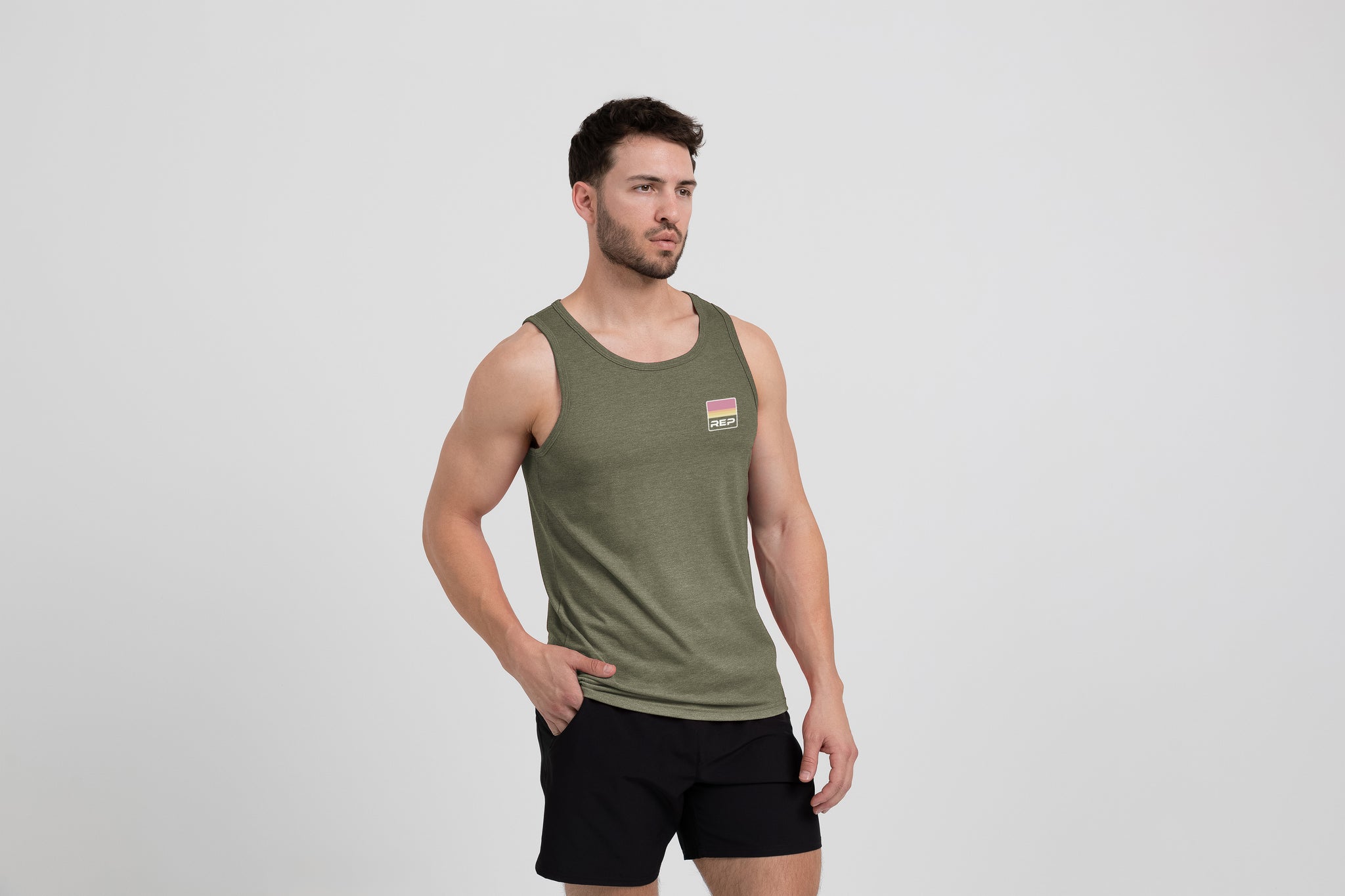 Man wearing an olive Men's Rise Tri-Blend Tank and shorts on a white background