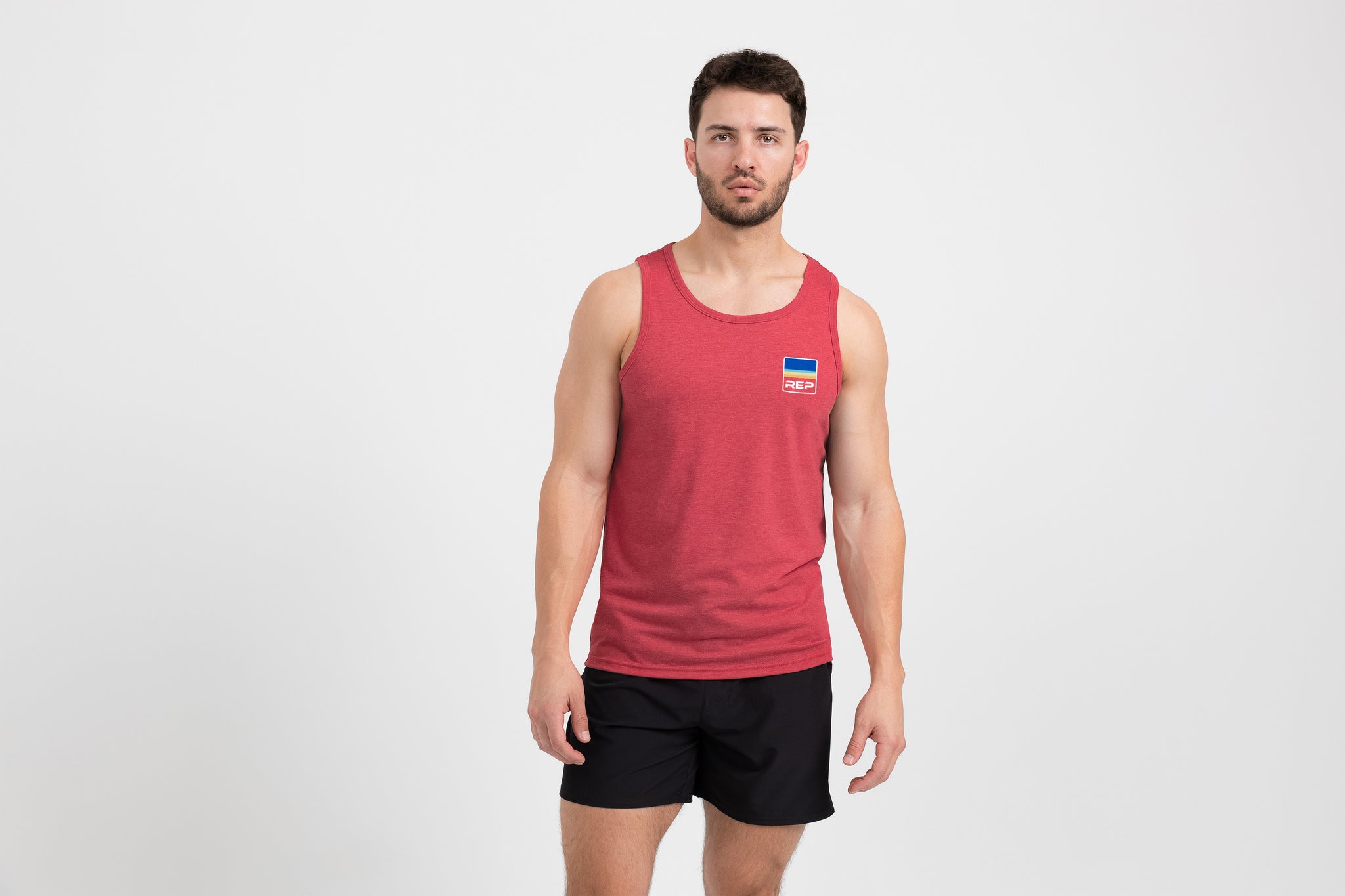 Man wearing a red Men's Rise Tri-Blend Tank and shorts on a white background