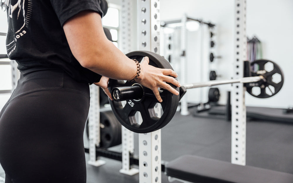 Female lifter loading a 25lb plate on a racked REP Mesa Technique Bar.