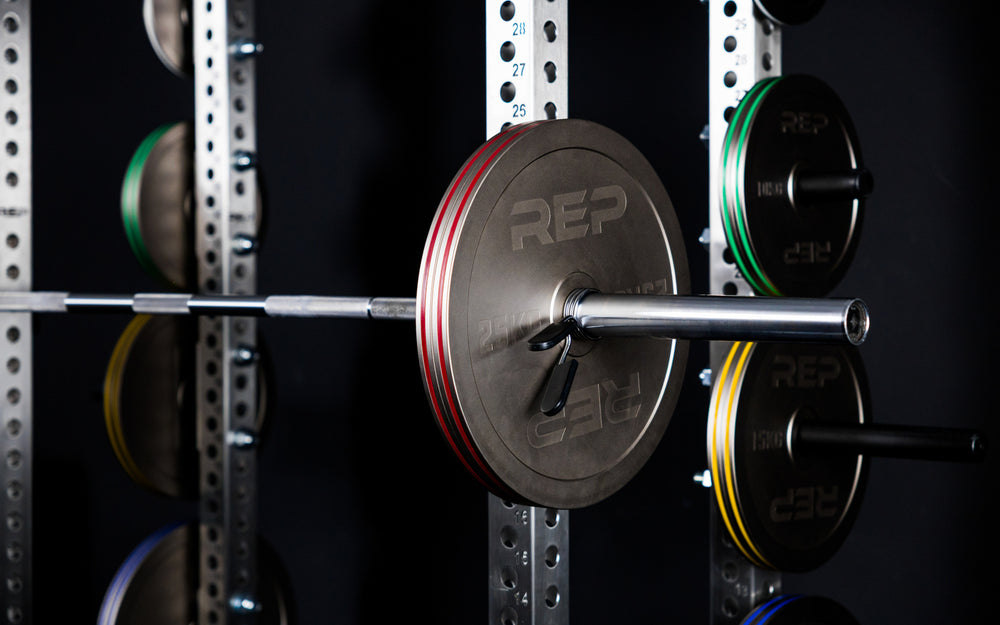Rep Fitness Calibrated Steel Plates (KG) loaded on a barbell and on weight horns on a PR-5000 rack, highlighting their colored banding