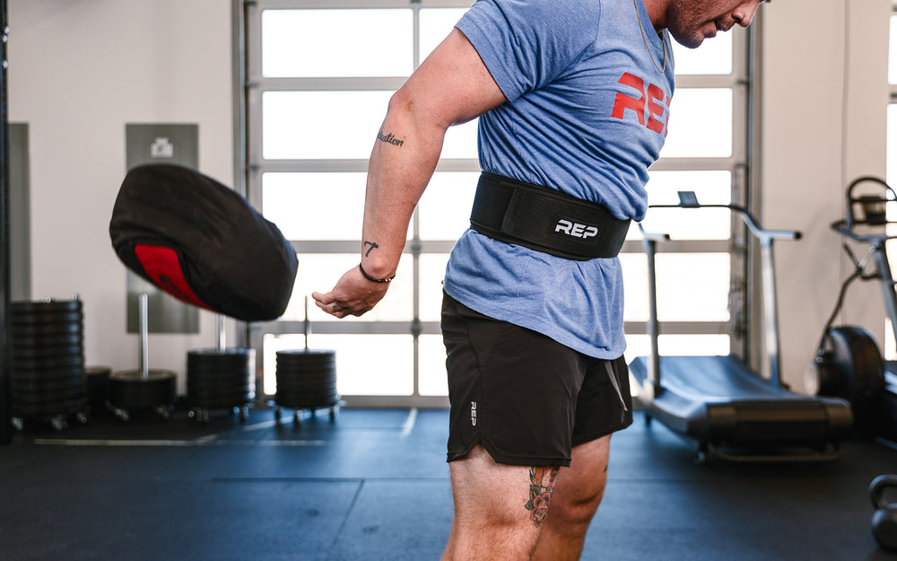 Athlete performing a ground to over the shoulder lift with a REP Stone Sandbag while wearing a REP Nylon Lifting Belt.