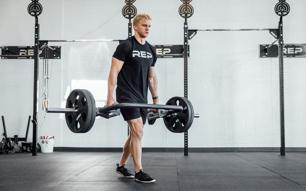 Male athlete performing a farmers carry with the REP Open Trap Bar.