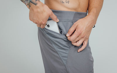 Close-up view of model sliding his iPhone into the side pocket of his "Cool Gray" REP Pinnacle Shorts.