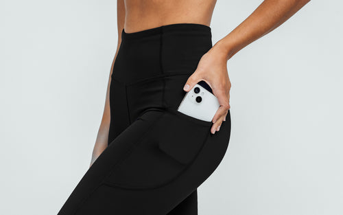 Close-up view of model sliding her iPhone in the side pocket on the black REP Hera Tights.