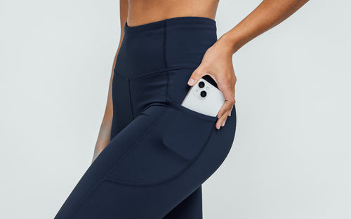 Close-up view of model sliding her iPhone in the side pocket on the navy REP Hera Tights.