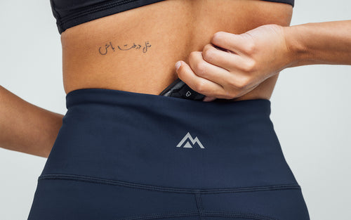 Close-up view of model sliding her keys in the rear pocket on the navy REP Hera Tights.