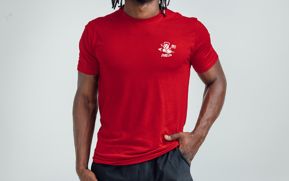 Model posing with a front view of the REP Men's Liberty Bell Tri-Blend Crew T-Shirt in Red and graphic in White