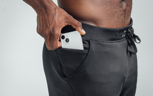 Close-up view of model sliding his iPhone in the zippered high hip pocket of his REP Attis Shorts.