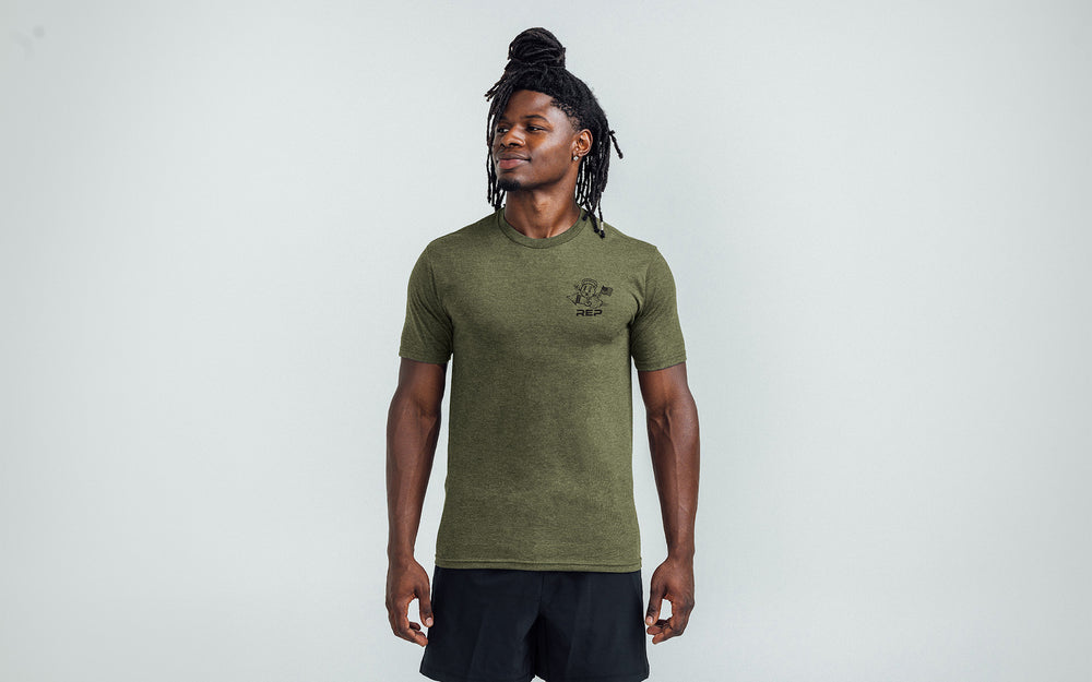 Model posing with a front view of the REP Men's Liberty Bell Tri-Blend Crew T-Shirt in Olive and graphic in Black