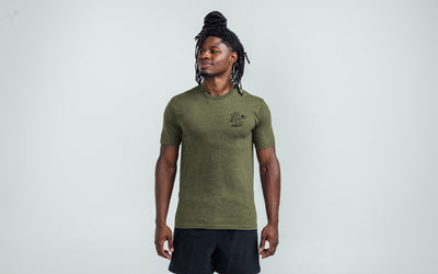 Model posing with a front view of the REP Men's Liberty Bell Tri-Blend Crew T-Shirt in Olive and graphic in Black