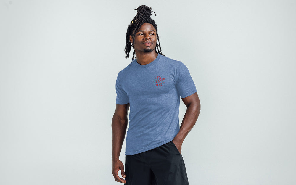 Model posing with a front view of the REP Men's Liberty Bell Tri-Blend Crew T-Shirt in Blue and graphic in Red